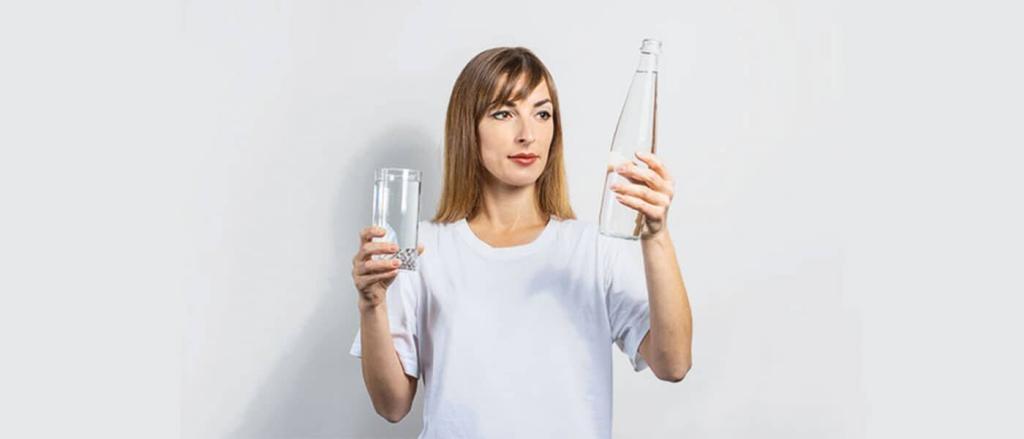 Mineralwasser vs. Leitungswasser: Junge Frau mit Flasche und Glas in der Hand